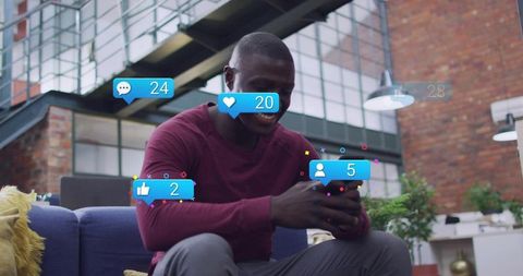 Smiling man holding smartphone on sofa with social engagement overlays in modern loft