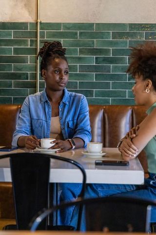 African american women sharing serious conversation over coffee in modern green-tiled cafe
