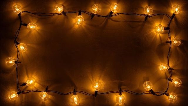 Amber globe filament string lights casting warm golden glow on dark textured wall frame