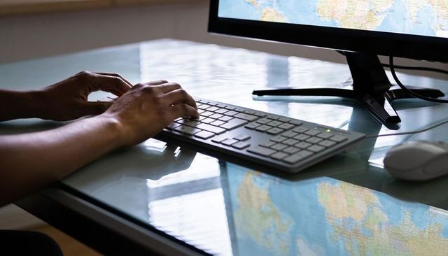 Typing on white keyboard with world map on monitor and glass desk reflection