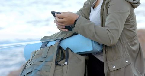 Traveler with backpack texting by rocky lakeside