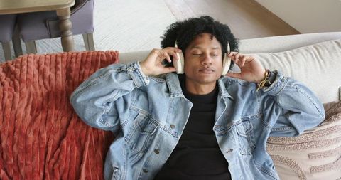 African american man relaxing on couch with headphones and denim jacket listening to music