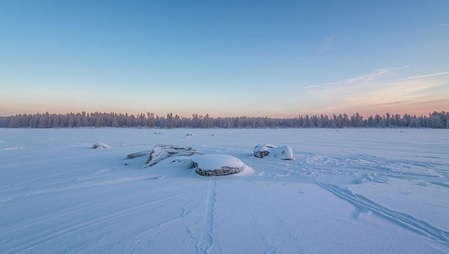 Snow-covered boulders on frozen lake at sunrise with frosted forest horizon