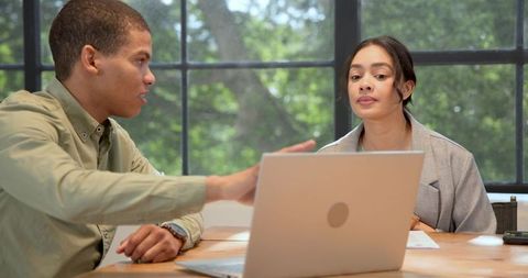 Diverse coworkers reviewing laptop and documents while collaborating at modern office table