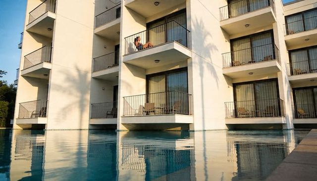 Relaxing guest reading phone on balcony over reflecting resort pool at golden hour
