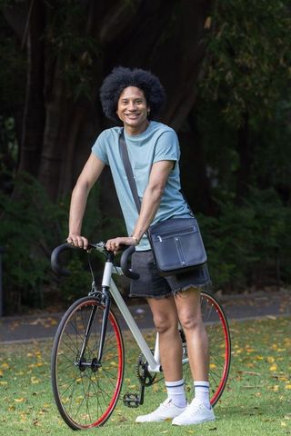 Smiling african man standing with road bike in urban park wearing crossbody bag