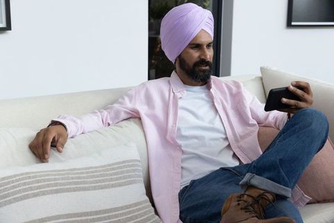 Indian Man Relaxing on Sofa with Smartphone in Modern Living Room