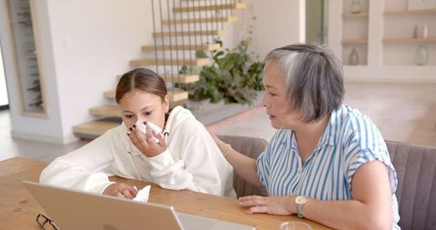 Grandmother comforts anxious girl using laptop at home