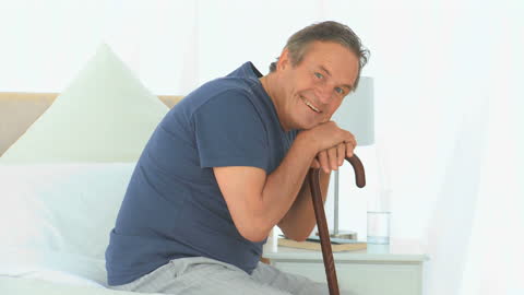 Elderly Man with Cane Smiling in Comfortable Bedroom