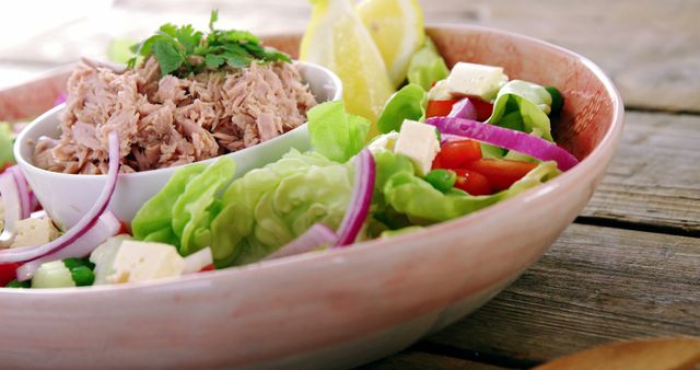 A bowl filled with a healthy tuna salad, featuring fresh vegetables, chunks of cheese, and a lemon wedge, with copy space. Its vibrant colors and arrangement suggest a focus on nutritious and appealing meal presentation.