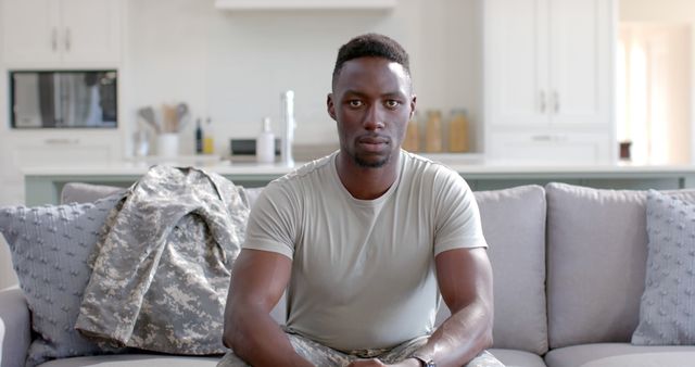 An African American soldier sits on a couch looking reflective at home, with his camouflage uniform beside him. This can be used for content on military experiences, veteran stories, transitioning to civilian life, and motivational or inspirational pieces. Suitable for articles, social media posts, and ads focusing on the challenges and strength of military personnel.