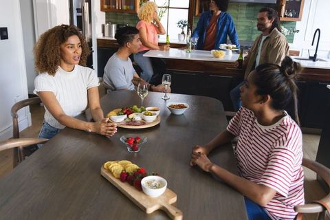 Diverse friends socializing around long wooden dining table in warm rustic kitchen