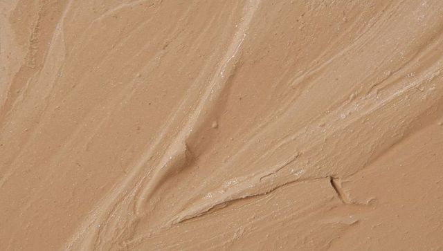 Spreading beige cream with spatula strokes, glossy viscous cosmetic texture
