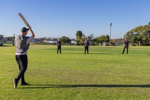 Men playing cricket on sunny neighborhood field with batsman raising bat mid-swing