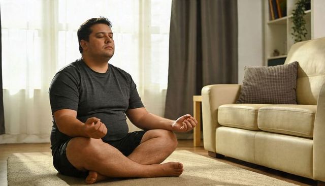 Mindful man meditating cross-legged on living room rug near sofa and sunlit sheer curtains