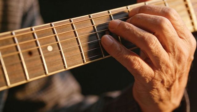 Pressing hand forming chord on acoustic guitar fretboard with warm woodgrain closeup
