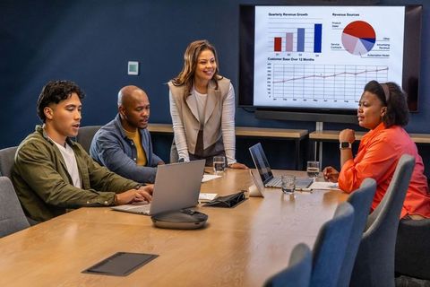 Diverse team collaborating in modern conference room presenting quarterly growth charts