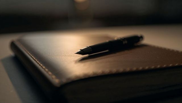 Resting leather journal with stitched edge and black fountain pen on desk in warm bokeh