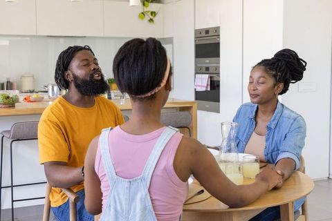 African american family holding hands praying at kitchen table