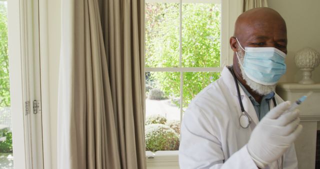 African american senior male doctor wearing face mask holding a syringe of covid-19 vaccine at home. vaccination for prevention of coronavirus outbreak concept