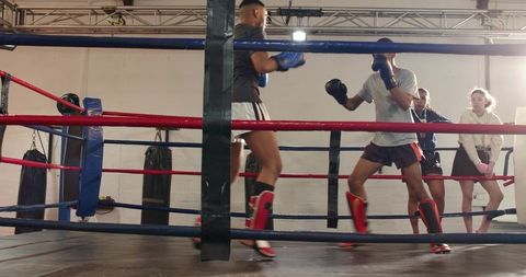Two fighters sparring in boxing ring during intense gym training with coach observing