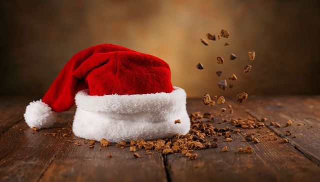 Santa hat on rustic wooden table with falling cookie crumbs and warm bokeh