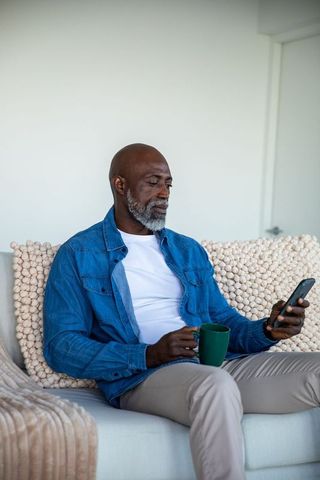 Senior African American Man Relaxing with Coffee and Smartphone at Home