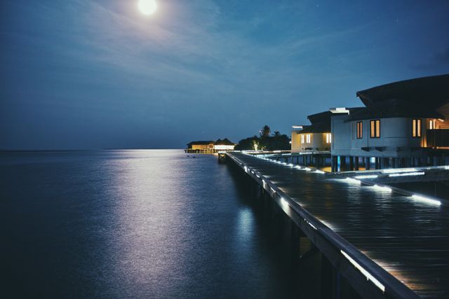 Moonlit tropical resort with over water bungalows under a serene night sky, ideal for promoting luxury vacation packages, travel brochures, romantic getaways, and tranquil holiday destinations.