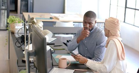 Colleagues discussing work in modern office with tablet and laptop