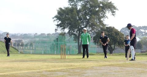 Cricket Players Practicing Bowling and Batting on Grassy Field