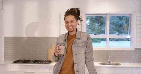 African American man smiling and leaning on kitchen counter holding coffee mug