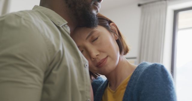 Image of happy diverse couple embracing with eyes closed and smiling at each other at home. Domestic life, love, togetherness, health, happiness and inclusivity concept.