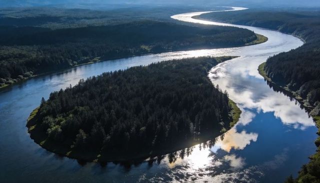 Meandering river encircling dense conifer peninsula with mirror-like water reflections