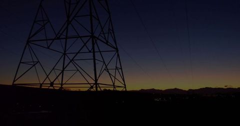 Looming Transmission Tower Silhouette at Dusk Sending Power Lines Across Mountain Horizon