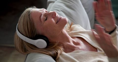 Relaxing senior woman enjoying music with wireless headphones at home