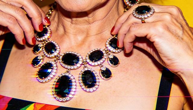 Senior woman adjusting statement necklace with red nails bold ring, luxe jewelry closeup