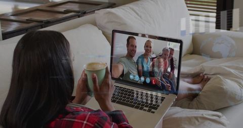 Woman enjoying cozy multigenerational family video call on laptop with coffee on sofa