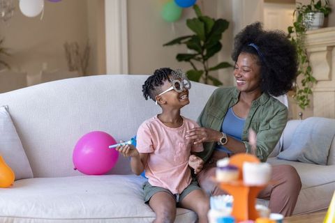 African american mother laughing with son on sofa celebrating 100th-day party at home