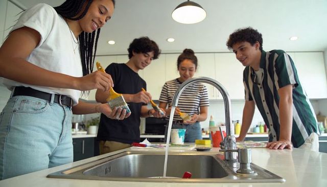 Teens collaborating on vibrant painting project at kitchen island with running faucet