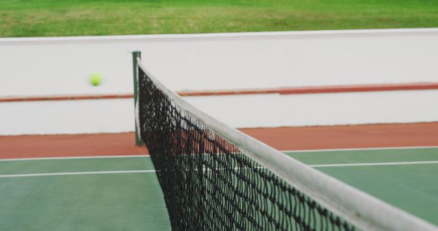 This closeup depicts a tennis ball in motion, focused on the net and court. Ideal for sports promotions, fitness campaigns, competition-themed posters, or websites featuring outdoor activities and tennis.