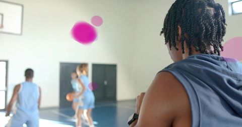 Standing player watching teammates dribbling on indoor basketball court