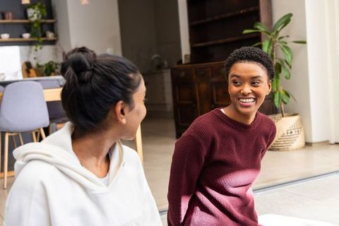 African american woman laughing, indian woman chatting in modern open-plan living space