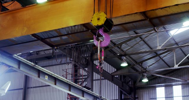 An industrial crane hook hangs inside a warehouse. Heavy machinery is essential for lifting and moving large loads in such settings.