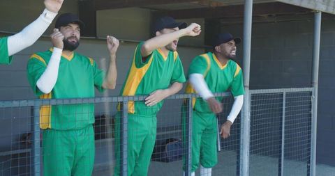 Cricket players cheering in dugout wearing green uniforms shouting and urging teammates