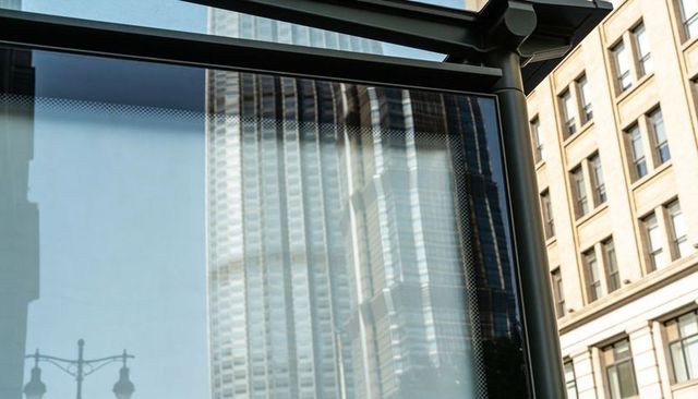 Skyscraper reflecting on glass transit shelter with metal frame and historic facade