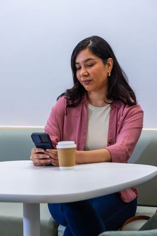 Checking flip phone while having coffee in minimal cafe lounge, casual mobile lifestyle