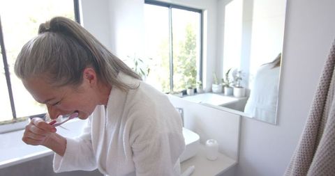 Mature Woman Brushing Teeth in Bright Bathroom
