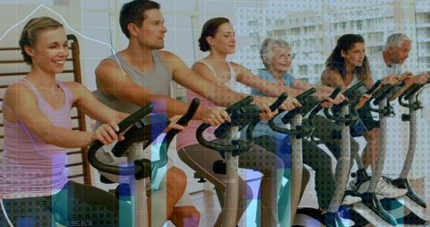 Group Spinning Class Pedaling on Stationary Bikes with Digital Fitness Overlay