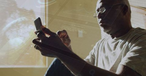 Senior man using smartphone by sunlit window with HUD overlay, glasses and wedding ring