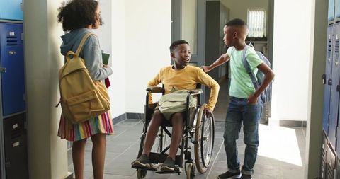 African american students chatting in school hallway with friend using wheelchair